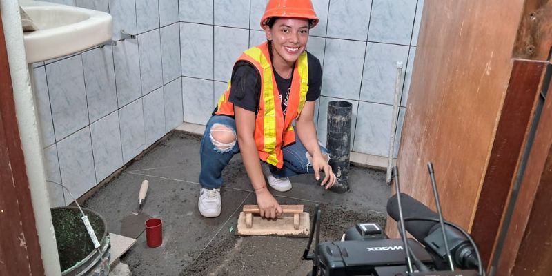 mujer con chaleco anaranjado trabajando con concreto 