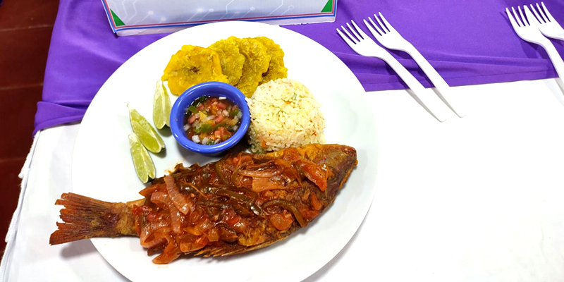 Pescado frito en salsa con arroz y tostones en un plato blanco